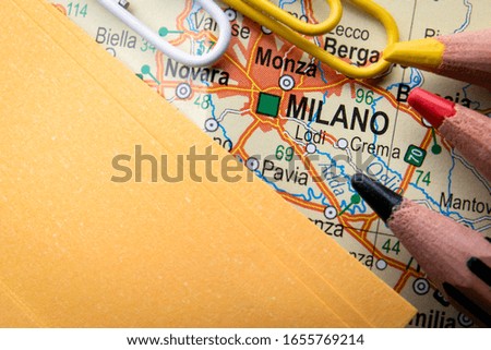 Milano city of  Italy in the center of the geographic map, pencils and paper sheet
