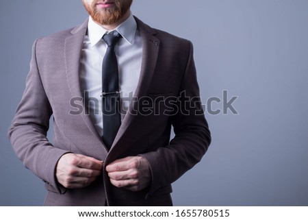 studio portrait of a young bearded handsome guy of twenty-five years old, in an official suit, buttoning a button in a jacket. On a dark background. Office Style. Fashion and office