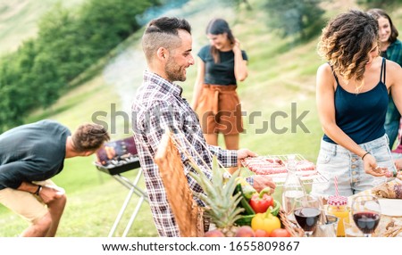 Young friends having fun on outdoors picnic preparing food at barbecue grill party - Happy people cooking and eating at countryside open air restaurant - Youth friendship concept on bright warm filter