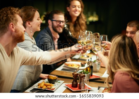 Best friends sitting in restaurant for dinner and making a toast with white wine. On table is food. Royalty-Free Stock Photo #1655839093