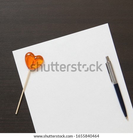 Template of white paper with pen and heart shaped caramel on dark wenge color wooden background. Concept of entertaining children's business, leisure for kids. Stock photo with empty space for text.