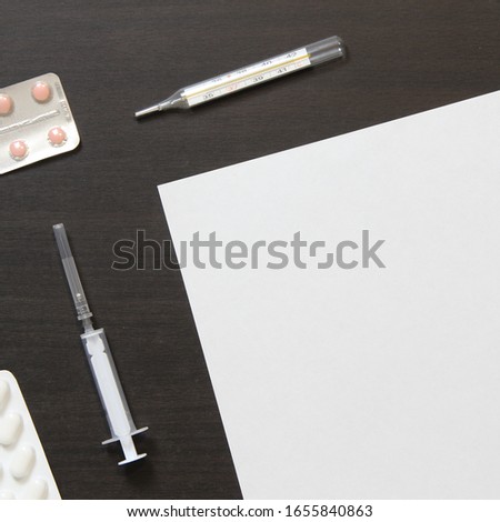 Template of white paper with pills in a blister, thermometer and syringe for injection on dark wenge color wooden background. The provision of medical and pharmacological services. 