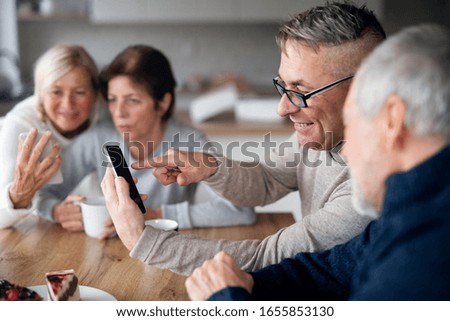 Group of senior friends at home, using smartphones.