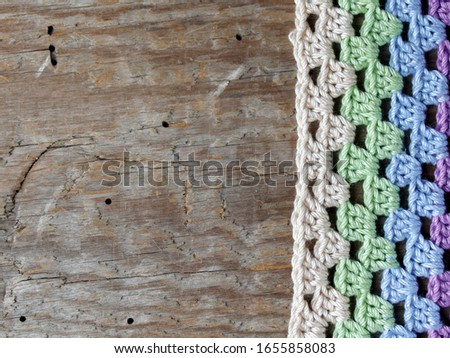 Crocheted element of green, purple, blue, beige flowers on an old wooden natural background. Screensaver for the desktop. Needlework, handmade, hobbies, free time.