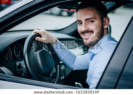 Young man smiling while driving a car looking at the camera Royalty-Free Stock Photo #1655858149