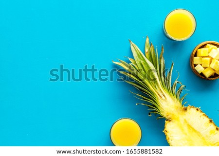 Pineapple juice on blue table with half of fruit top-down frame copy space