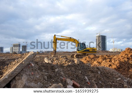 Yellow Excavator at building under construction. Backhoe digs the ground for the foundation and for laying sewer pipes. Renovation program. Buildings industry background