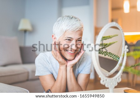 Cropped shot of a mature woman inspecting her skin in front of the mirror. Happy woman looking at herself in the mirror. Middele aged woman with face without wrinkles.
