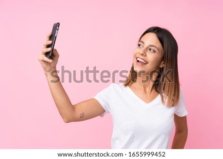 Young woman over isolated pink background making a selfie
