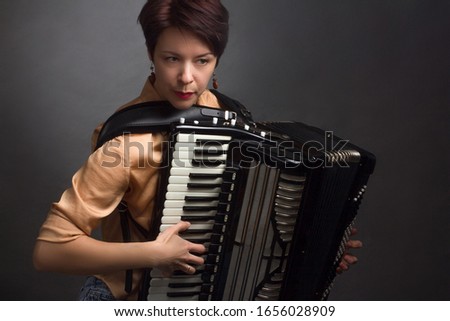 A brunette in a gold shirt, with a short haircut, on a light gray background of the Studio. play the accordion