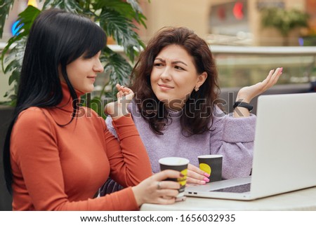 Picture of confused indignated friends making gestures, having unpleasant facial expression, sitting at table, drinking coffee, holding papercups with hot drink, being shocked with recent news.