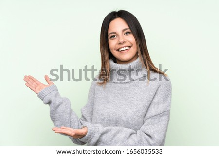 Woman wearing a sweater over isolated green background extending hands to the side for inviting to come