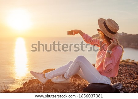 Tourist taking selfie on phone on Aegean sea background on Santorini island, Greece. Woman backpacker traveling