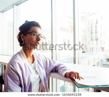 young cute indian girl at university building sitting on stairs reading a book, wearing hipster glasses, lifestyle people concept close up