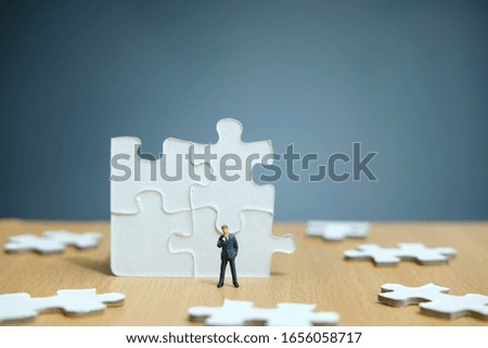 Conceptual photos of business strategies - Miniature entrepreneurs stand and think in front of 4 jigsaw puzzles that are arranged