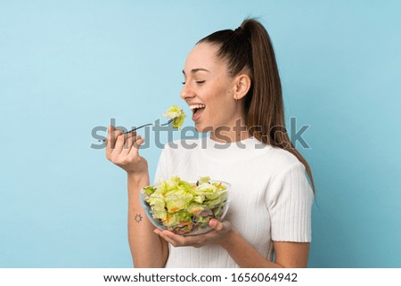 Young brunette woman holding a salad over isolated blue background