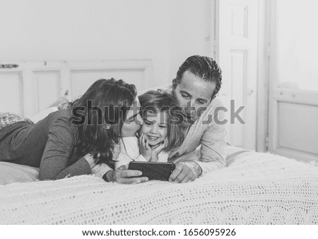 Happy family watching video on the internet on mobile phone in bed at home. Mom dad and little daughter girl playing on smartphone having fun together. In Education, digital generation and technology.