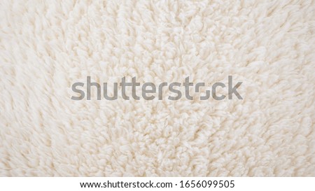 Background picture of a soft fur white carpet. wool sheep fleece closeup texture background. Fake color beige fur fabric. top view.  Royalty-Free Stock Photo #1656099505