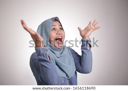 Portrait of happy muslim woman celebrating victory, winning gesture smiling and greeting something from above with copy space concept