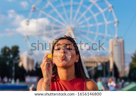 Beautiful young brunette woman blowing soap bubbles during sunset outdoors