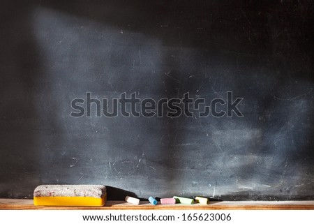 Blank blackboard with colored chalks and eraser and light effect. Horizontal composition. 