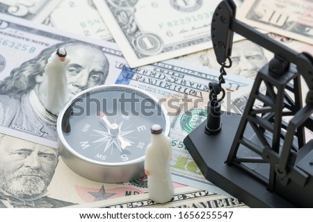 Oil pump jack and arab men looking at compass on US dollar bill banknotes background. Concept of OPEC crude oil production, petroleum exporting industry, petrodollar or commodity market investment.