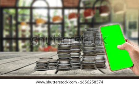 A pile of coins on a wooden table Hand holding phone screen green background blur