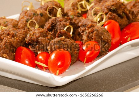 meatballs tomato on a plate board white toothpicks and lettuce close up focus