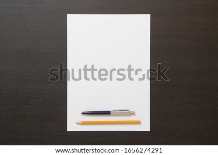 Template of white paper with pen and pencil on dark wenge color wooden background. Concept of business plan and strategy. Stock photo with empty space for text and design.