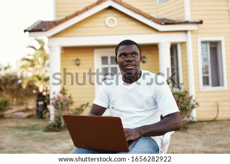 young dark-skinned man in a white t-shirt on the street with a laptop
