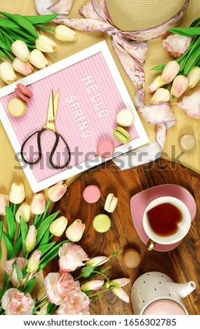 Hello Spring theme creative layout concept flat lay tea break with pink tulips and lisianthus flowers, sun hat on wooden table background, wih felt letter board.