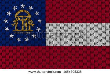 The national flag of the US state Georgia in against a gray textile material with sew thread on the day of independence in different colors of blue red and yellow. Clothing and industry.