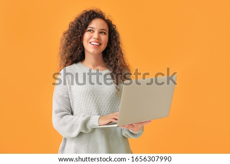 Young African-American woman with laptop on color background