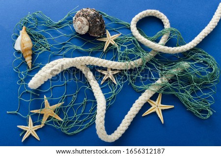 Closeup of fishing net, rope and seashell, starfish in it, blue surface.Concept of fish catching in the ocean