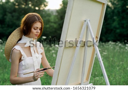 young easel woman paints a picture in the fresh air