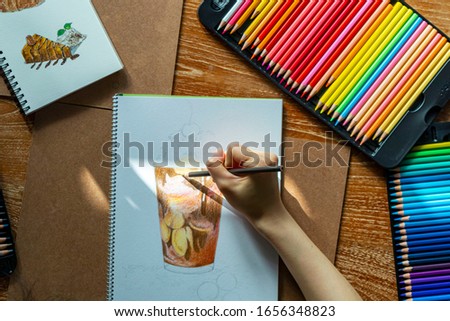Woman’s hand coloring chocolate milkshake with colorred pencils. Hand drawing. Banana chocolate smoothie in pencil color art. Artwork on white paper with natural light on the paper.