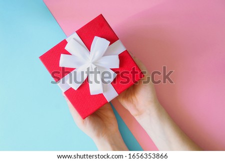 Woman holding red gift box on color blue and pink background. Festive greeting card. Holiday concept