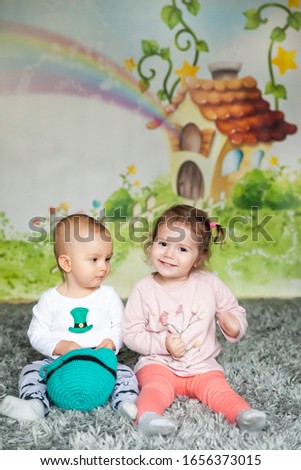 First birthday cute baby boy wearing a St. Patrick's Day hat and his sister. Cartoon fairy house on background
