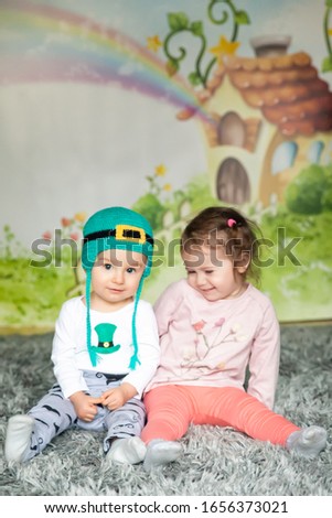 First birthday cute baby boy wearing a St. Patrick's Day hat and his sister. Cartoon fairy house on background