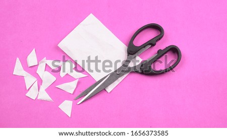 Black scissor cutting white paper on pink background.