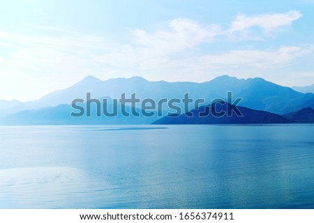 Tranquil landscape of mountains and lake water in the sunrise lights. Morning fog over the water surface. Skadar lake, Montenegro. Nature background Royalty-Free Stock Photo #1656374911