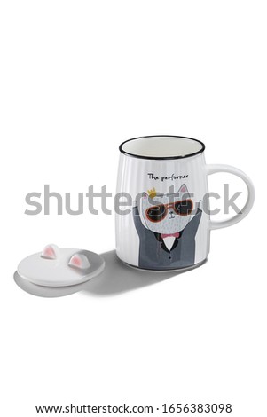 Subject shot of a white ceramic mug with a picture of a dressed up cat in sunglasses and lettering "The performer". The cup and a cover with cat's ears are isolated on the white background. 