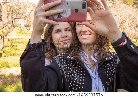 two girls taking pictures in a park full of flowering trees