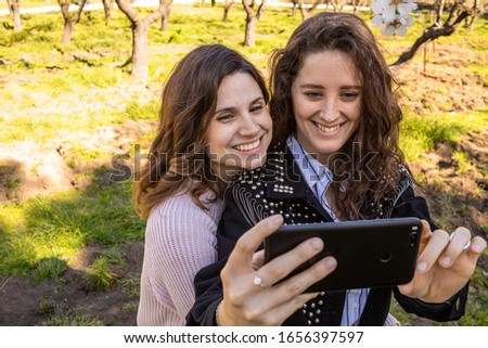 two girls taking pictures in a park full of flowering trees
