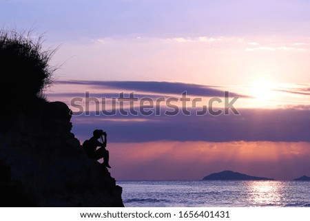 A man standing with a camera on a cliff by the sea at sunrise blue sky background.
