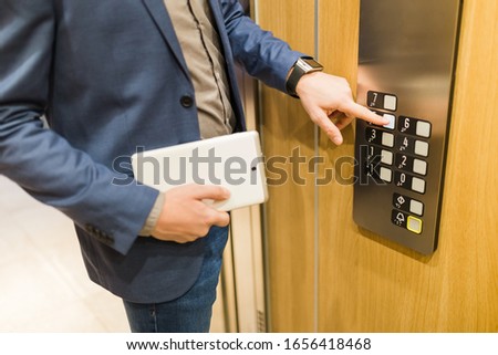 Close up of businessman with tablet device pressing elevator button. Business and office building meeting concept.