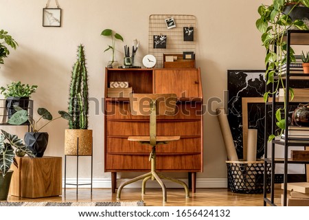 Retro interior design of art workshop room with wooden vintage bureau and chair, shelf plants, cacti, books, photos and elegant personal accessories. Stylish vintage home decor. Beige wall. Template. 