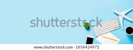 Keyboard, flower, airplane, cup with tea or coffee, a blank sheet and a pencil on a blue background. Concept of travel planning, buying airline tickets online, air tickets. Banner. Flat lay, top view