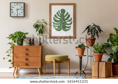 Vintage interior design of living room with stylish retro furnitures, a lot of plants, commode, black clock and brown poster mock up frame on the beige wall. Stylish home decor. Template. 
