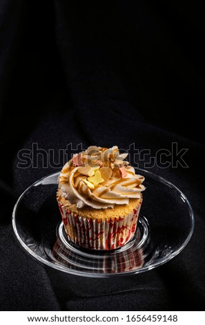 One vanilla cupcake with buttercream icing and decoration on transparent saucer isolated on black